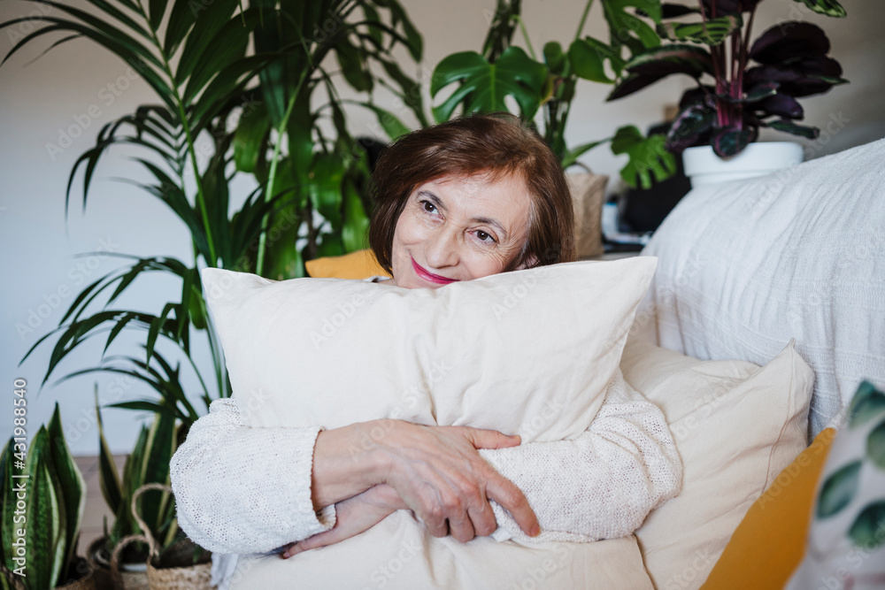 Smiling woman embracing cushion sitting on sofa at home Smiling woman embracing cushion sitting on sofa at home