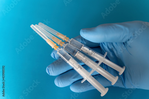 Hand of person wearing protective glove holding three syringes photo