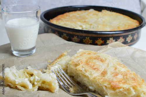 Traditional Balkan, Serbian cheese pie, burek, borek on the paper, with glass of yogurt in the background, closeup photo