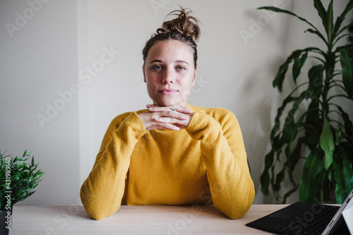 Confident woman with hand on chin staring while sitting by table at home photo