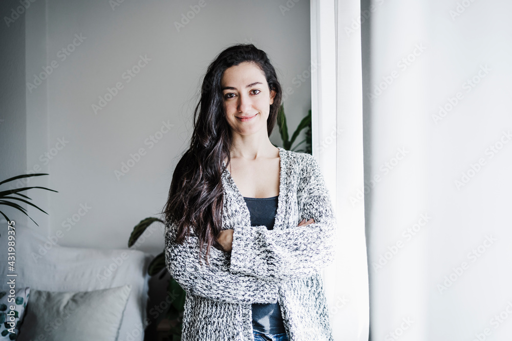 Smiling woman with arms crossed standing against wall in living room