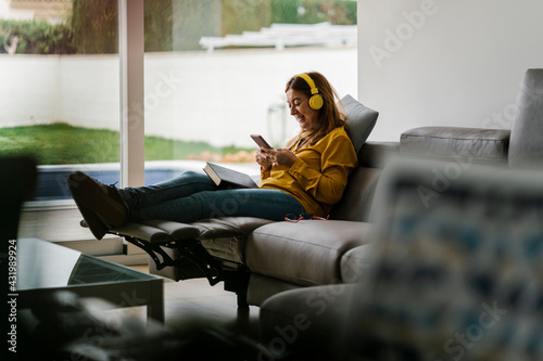 Mature woman listening music while sitting on reclining chair in living room