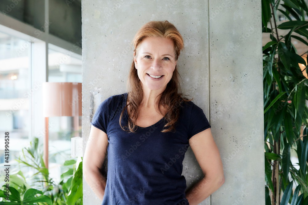 Mature woman with hands behind back standing against column in loft apartment at home Mature woman with hands behind back standing against column in loft apartment at home