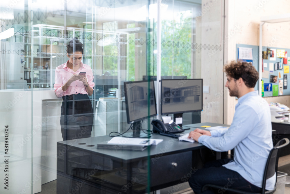 Young male entrepreneur working while female colleague using smart phone at office Young male entrepreneur working while female colleague using smart phone at office