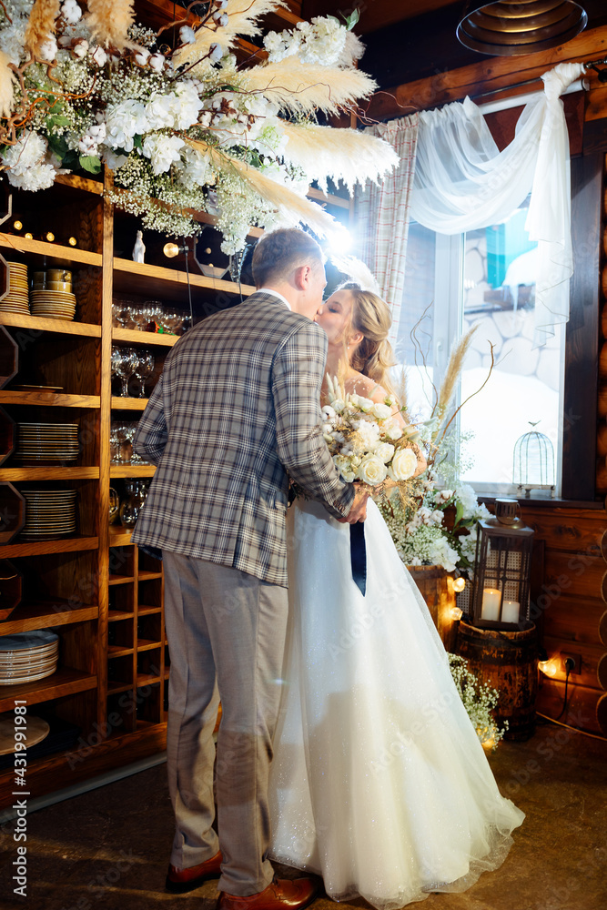 Wedding ceremony of the groom in a tuxedo and the bride in a white dress. Couple looks at each other and kisses against the background of a wedding arch indoors with dried flowers Wedding ceremony of the groom in a tuxedo and the bride in a white dress. Couple looks at each other and kisses against the background of a wedding arch indoors with dried flowers