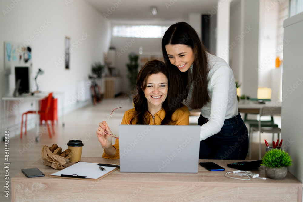 Smiling mother and daughter working on laptop at desk in home office Smiling mother and daughter working on laptop at desk in home office