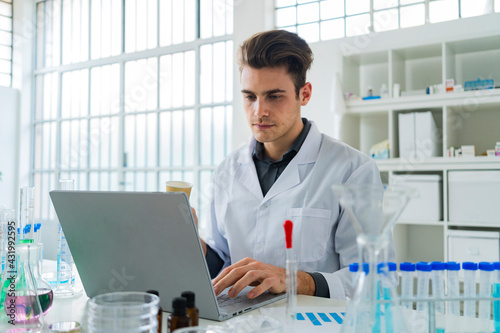 Serious male scientist working on laptop while sitting at desk in laboratory