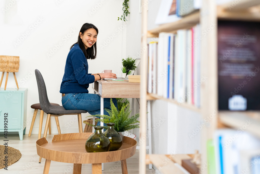 Woman smiling while sitting by laptop on table at home office Woman smiling while sitting by laptop on table at home office