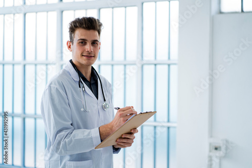 Young doctor writing notes while holding clipboard in hospital