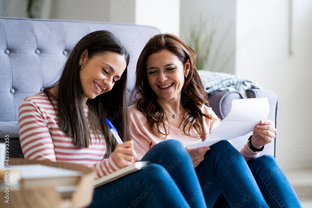 © Giorgio Fochesato/Westend61 - Smiling mother and daughter checking bills while sitting by sofa in living room