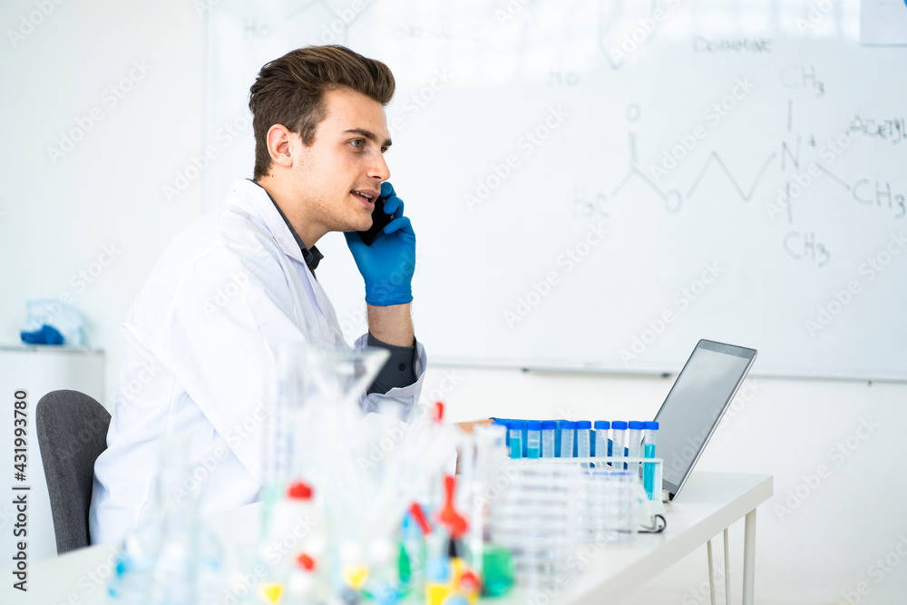 Male scientist talking on mobile phone while sitting at desk in laboratory Male scientist talking on mobile phone while sitting at desk in laboratory