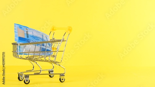 Shopping cart with 2000 rubles banknote on a yellow background, closeup. Black Friday Shopping and Discount Concept