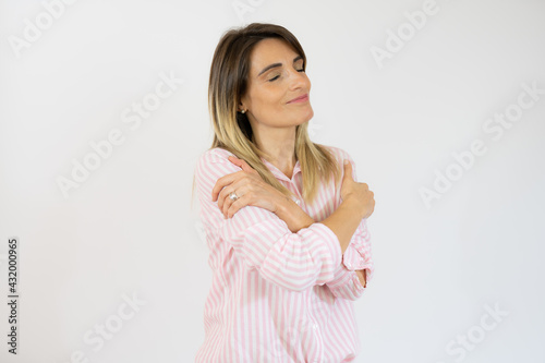 Smiling woman in striped shirt hugging herself isolated over white background.