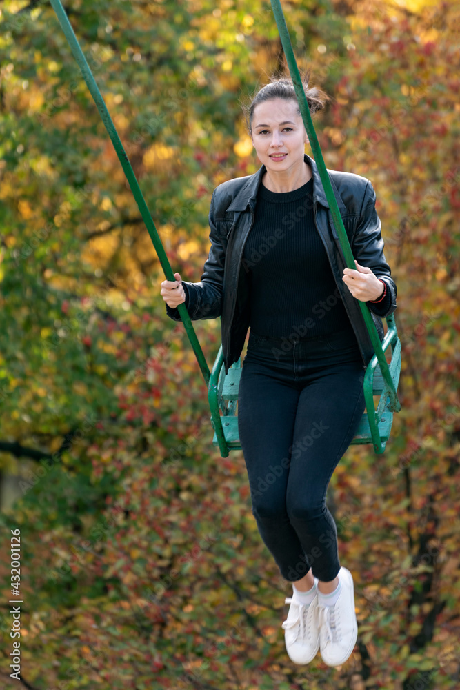 Young cheerful woman goes for a drive on swing in autumn park. Vertical frame