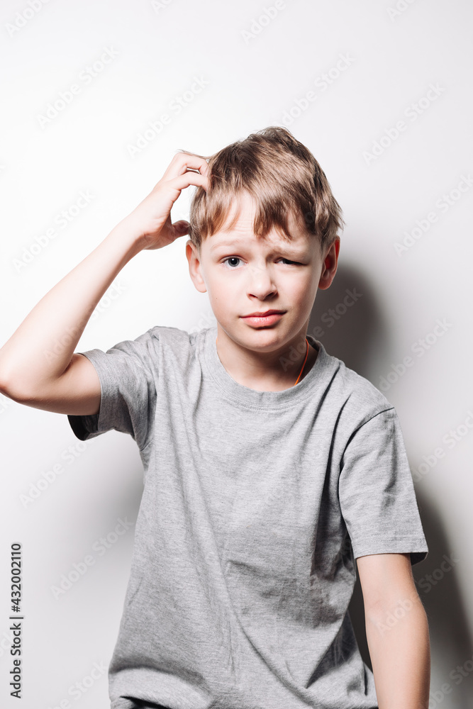 boy with blond hair shows bewilderment on his face and scratches the back of his head on a white background boy with blond hair shows bewilderment on his face and scratches the back of his head on a white background
