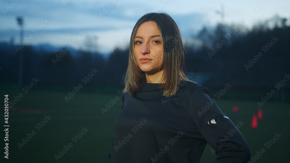Portrait of young woman soccer player standing on grass field at night.