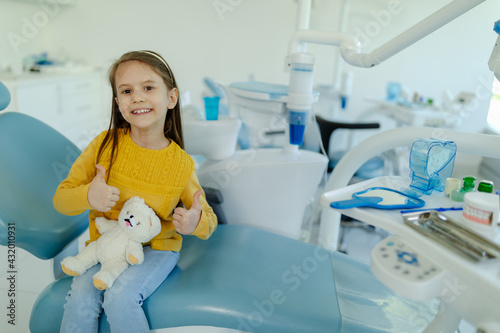 Little girl sitting on a chair in a dental office  showing thumbs up after a dental examination.