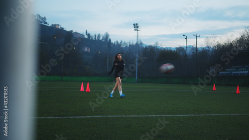 Fototapeta Naklejka Na Ścianę i Meble -  Young female soccer player kicking ball into goal from penalty marker. View from back of the goal.