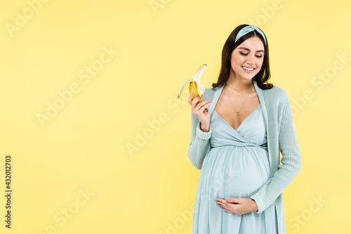 smiling pregnant woman holding ripe banana isolated on yellow.