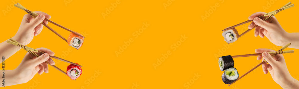 Obraz premium Women's hands hold sushi rolls with sticks. Yellow background. Creative concept