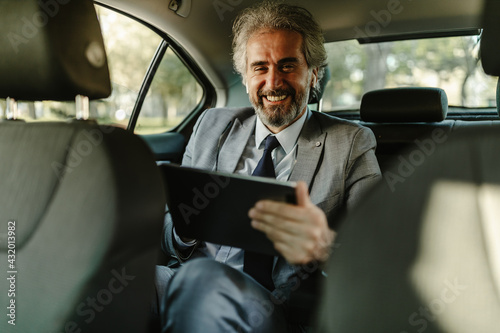 Close up photo of mature businessman in car working at digital tablet and looking at camera.