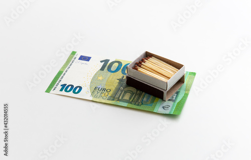 Matches in box are on 100 euro banknotes, box with red phosphorus made of wood, production of matchsticks, white background