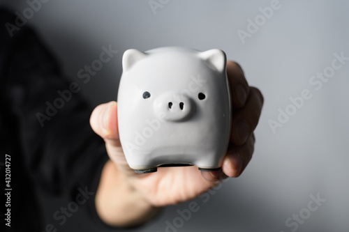 Hand holding white piggy shaped piggy bank on white background