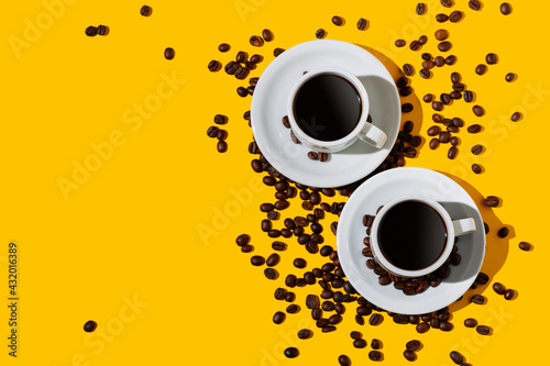 Top view of two coffee cup over a bright yellow color background and many beans spilled around. Flat lay photo with copy space.