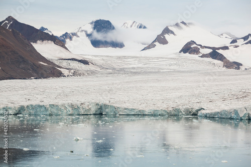 A small boat carrying out oceanographic surveys is dwarfed by the massive calving front of tidewater glacier Samarinbreen, Hornsund, Svalbard. photo