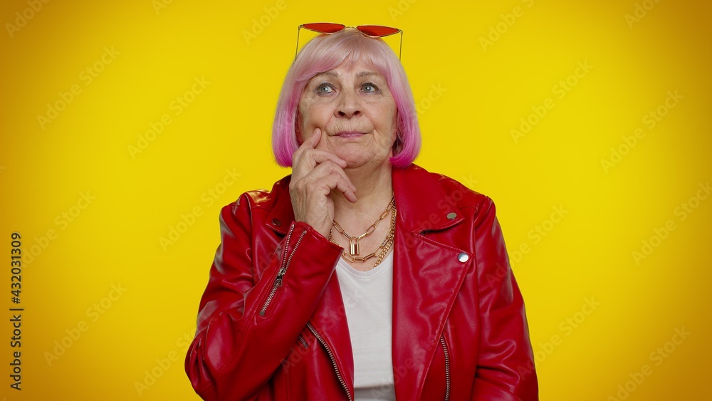 I need to think. Thoughtful clever senior rocker woman rubbing her chin and looking aside with pensive expression, pondering a solution, doubting question. Elderly grandmother on yellow background
