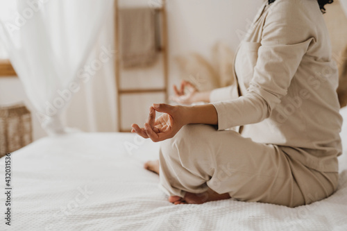 Cropped image of African-American woman practicing yoga and relaxation exercises on bed.