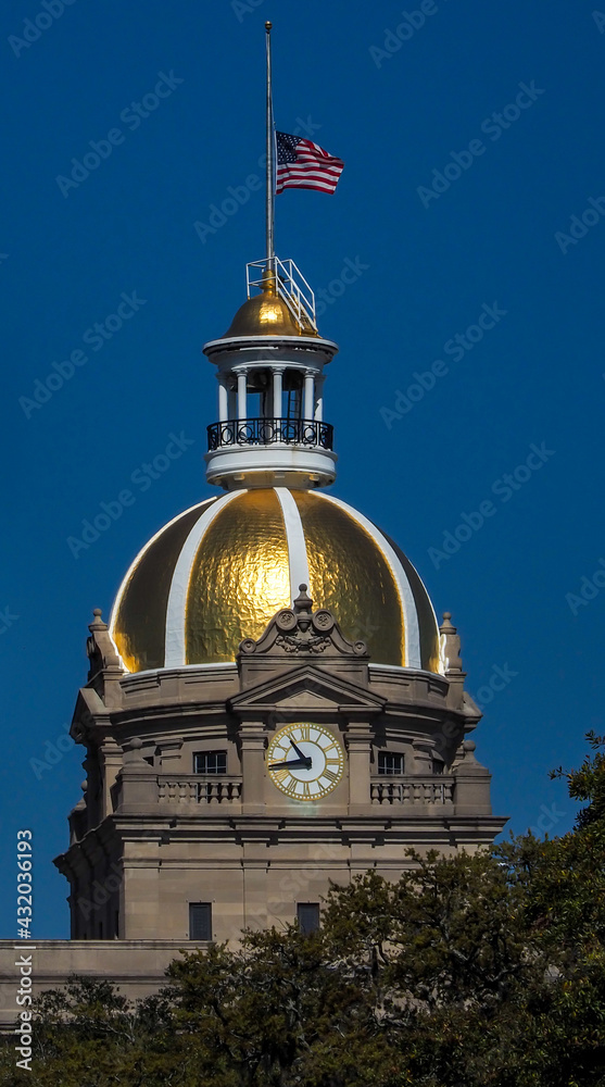 Ornate building with large clock and golden domed roof topped by flag at half staff