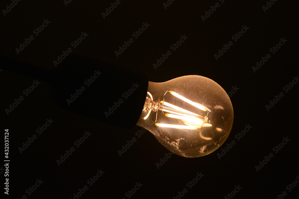 Stara i brudna  żarówka elektryczna słabo świeci żółtym światłem.  - obrazy, fototapety, plakaty 