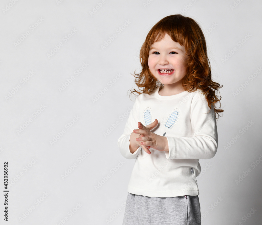 Charming cutie toddler smiling red-haired little girl in sportswear studio shot. Female child wearing white raglan with cute rabbit print design and sports pants. Headshot portrait isolated on white Charming cutie toddler smiling red-haired little girl in sportswear studio shot. Female child wearing white raglan with cute rabbit print design and sports pants. Headshot portrait isolated on white