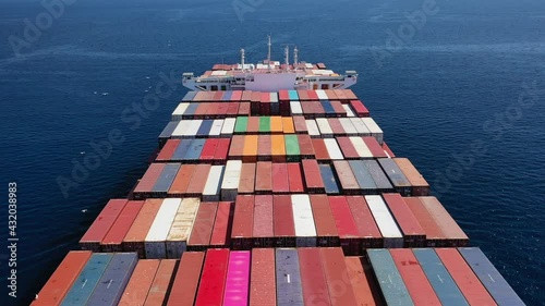Aerial drone flight above huge colourful container carrier ship cruising deep blue open ocean sea
