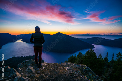 Adventurous athletic woman hiker standing on a mountain top watching the sunset over mountains and a beautiful lake. © Pelo Blanco Photo