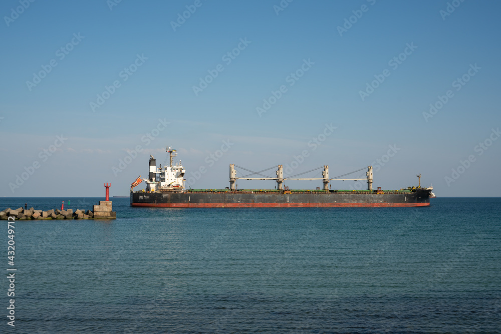 A large dry cargo ship leaves the port past the breakwater. A large dry cargo ship leaves the port past the breakwater.