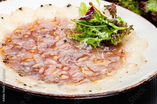 Seabass carpaccio served with arugula leaves, parmesan cheese and lettuce salad on white plate.