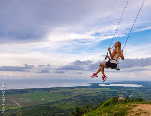 A young girl, blonde, swinging on a swing on a mountain slope in summer. Swing high in the mountains above the valley. Dominican Republic. Setting sun