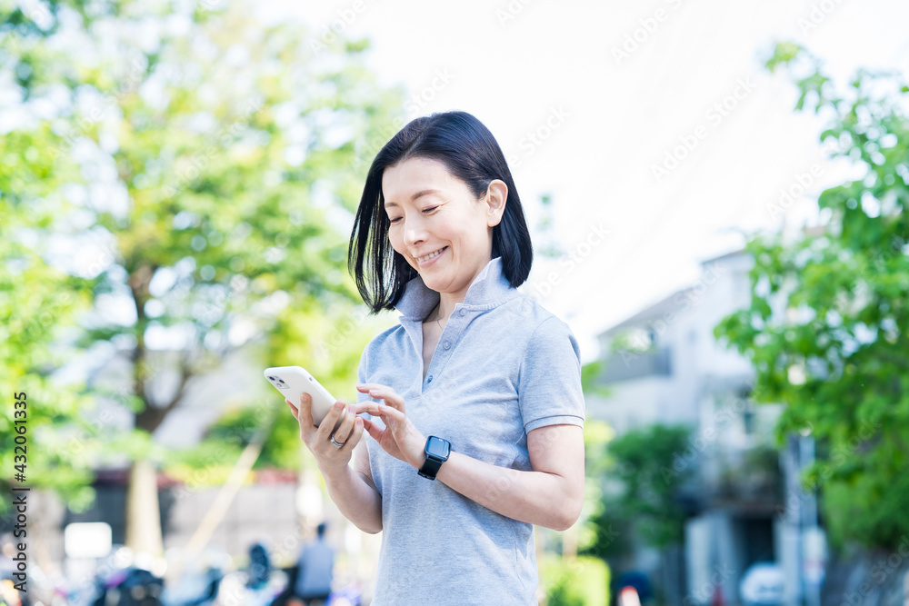 屋外でスマートフォンを操作する中年女性 屋外でスマートフォンを操作する中年女性