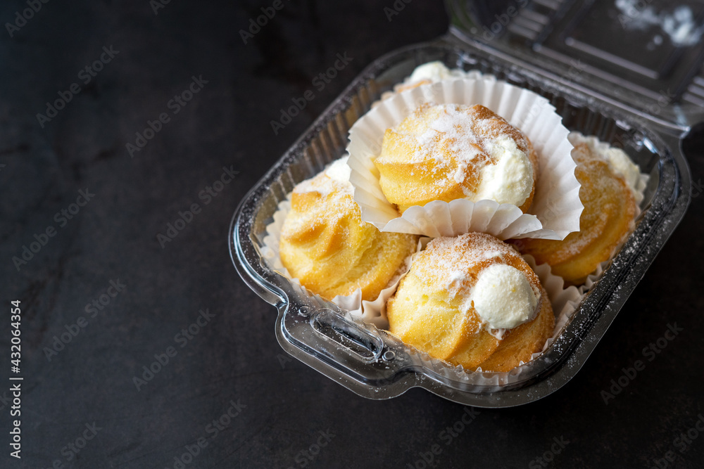 Cream puffs filled with pastry cream and sprinkled with powdered sugar in a transparent clear container. Cream puffs filled with pastry cream and sprinkled with powdered sugar in a transparent clear container.
