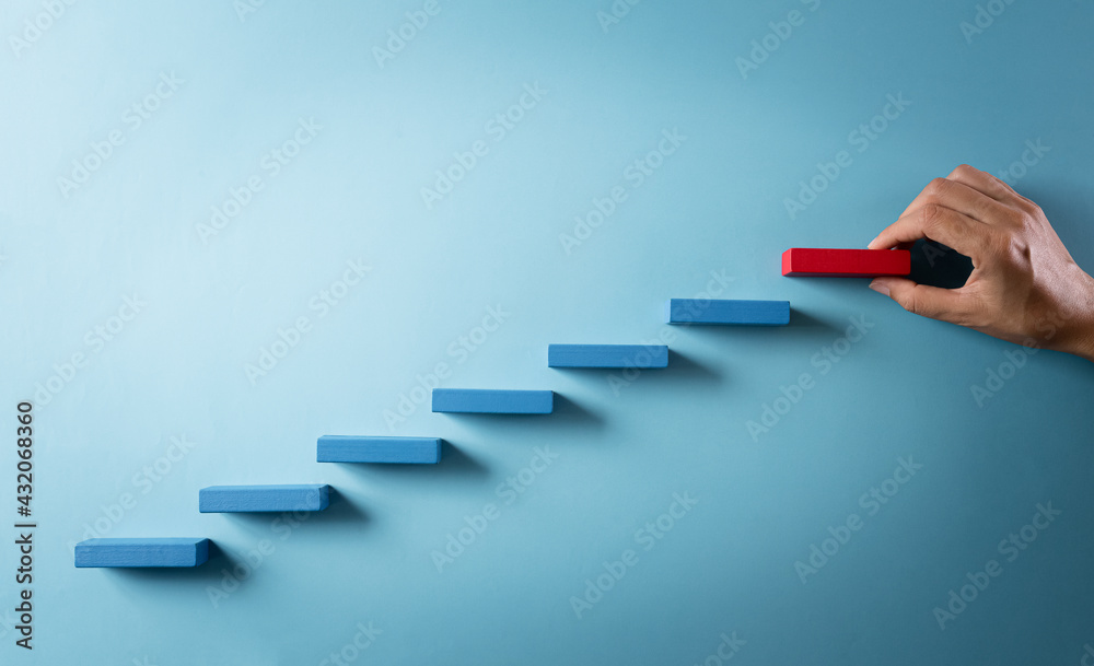 Concept of building success foundation. Hand holding wooden block stacking as step stair, Success in business growth concept on pastel background.