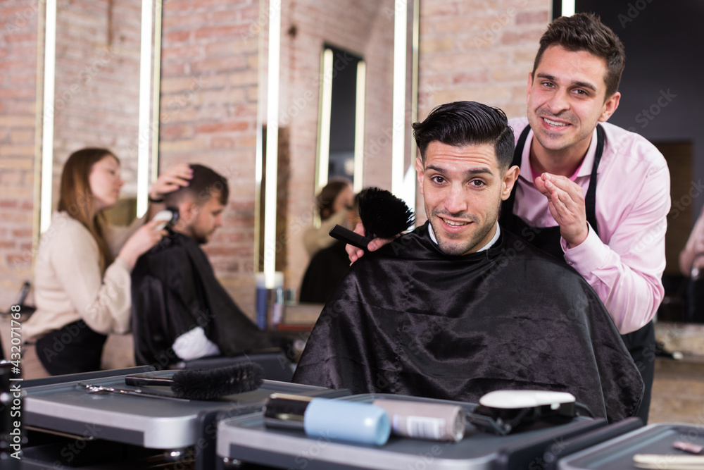 Obraz premium Portrait of skilled hairstylist and satisfied male customer after haircut in modern hair studio