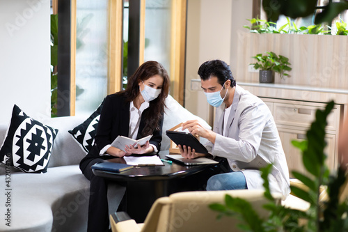 Beautiful woman real estate agent offering and showing online presentation on laptop in office to handsome man. People wearing face mask protective corona virus.