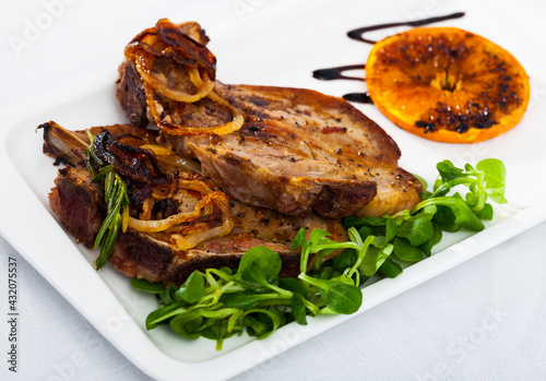 Roasted pork cutlets with fresh greens and grilled orange on white plate