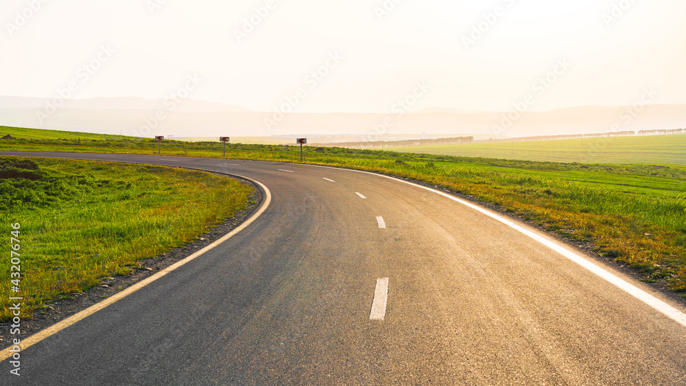 Asphalt road between green farm fields with blue sky and clouds Asphalt road between green farm fields with blue sky and clouds
