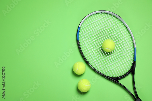 Tennis racket and balls on green background, flat lay. Space for text