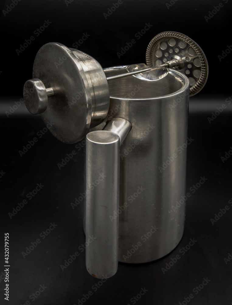 Cafetiere plunger is placed on stainless steel jug with black background. French press coffee. Abstract metalwork of Cafetiere like a weightlifter. Selective focus. Cafetiere plunger is placed on stainless steel jug with black background. French press coffee. Abstract metalwork of Cafetiere like a weightlifter. Selective focus.