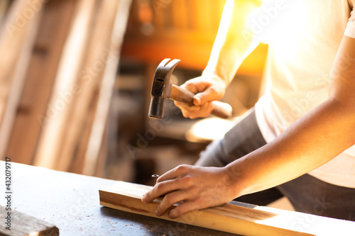 Close up of carpenter hammering a nail into wooden board. Construction industry concept.