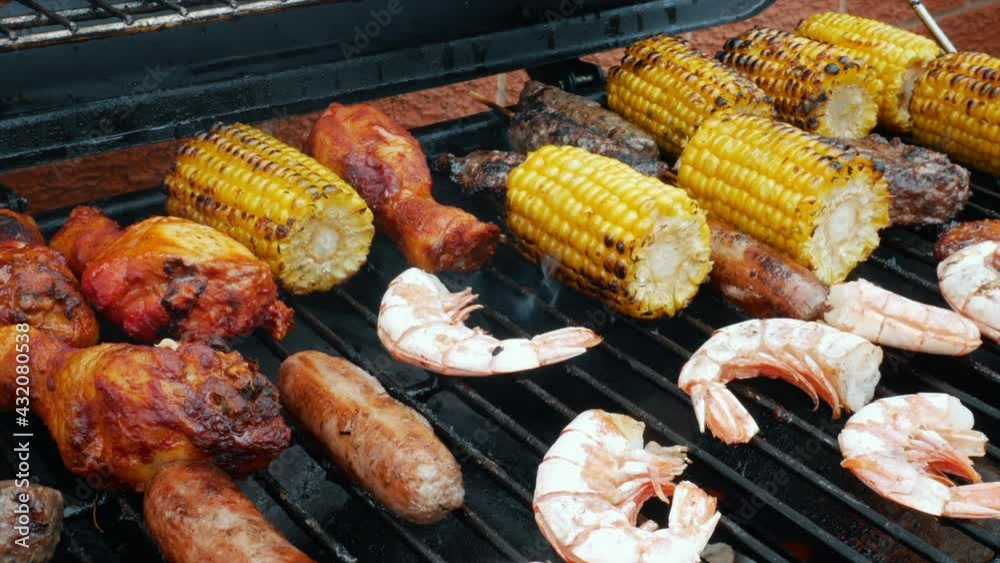 Mixed meat and seafood barbecue. Grilled corn and chicken on bbq. The sausages and prawns grilling are sizzling on the barbie as a prawn is turned over. Mixed meat and seafood barbecue. Grilled corn and chicken on bbq. The sausages and prawns grilling are sizzling on the barbie as a prawn is turned over.